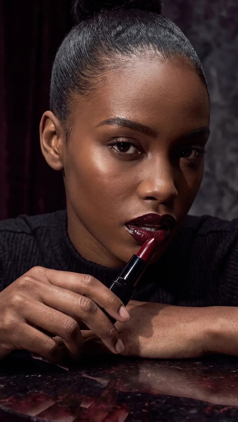 Synthetic adult beauty model with black-cherry lipstick beside a fictional black lipstick on obsidian